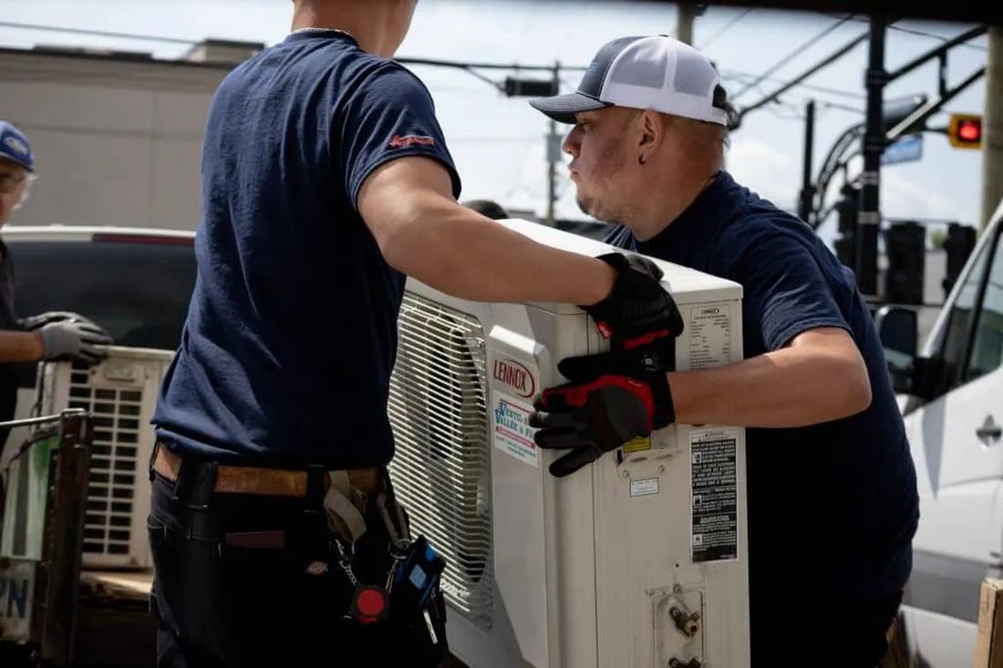 Technicians handling a new condensing unit at a job site